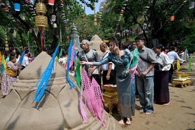 People throw sand on sand stupas as they pray during celebrations for the Khmer New Year, known as Nokor Sankranta, in Phnom Penh on April 15, 2026. (Photo by TANG CHHIN Sothy / AFP)