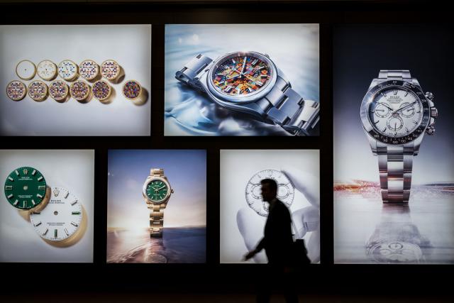 A visitor walks past photographs at the stand of Swiss luxury watchmaker Rolex during the opening day of the "Watches and Wonders Geneva" luxury watch fair, in Geneva, on April 14, 2026. The Geneva watch fair opened on April 14 and will be taken as a barometer of how the Middle East war is affecting the luxury goods sector. The Watches and Wonders salon -- the industry's biggest annual event -- sees 65 major watch brands, including Rolex, Patek Philippe, Cartier and Bulgari, display their latest creations until April 20. (Photo by Fabrice COFFRINI / AFP)