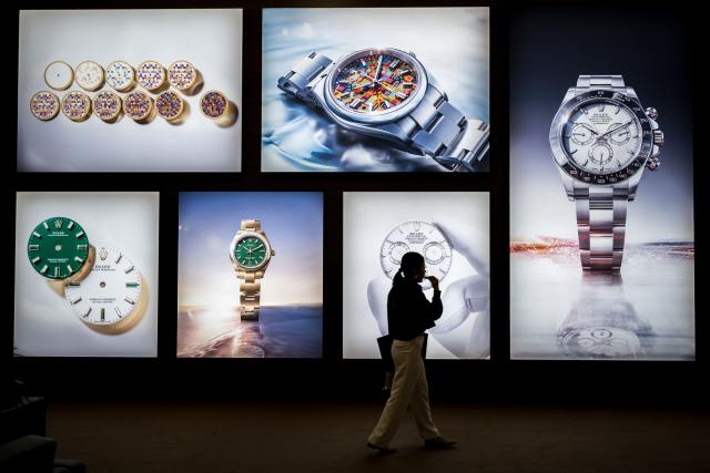 A visitor walks past photographs at the stand of Swiss luxury watchmaker Rolex during the opening day of the "Watches and Wonders Geneva" luxury watch fair, in Geneva, on April 14, 2026. The Geneva watch fair opened on April 14 and will be taken as a barometer of how the Middle East war is affecting the luxury goods sector. The Watches and Wonders salon -- the industry's biggest annual event -- sees 65 major watch brands, including Rolex, Patek Philippe, Cartier and Bulgari, display their latest creations until April 20. (Photo by Fabrice COFFRINI / AFP)