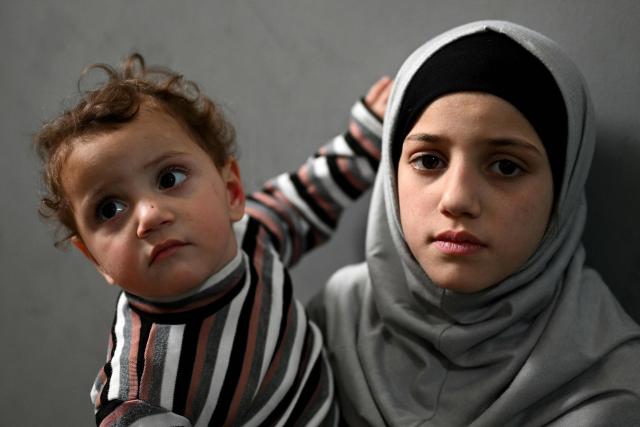 A displaced girl carries her brother at a corridor in a school transformed into a displaced reception center in the area of Dekwaneh, east of Beirut on April 15, 2026. United Nations refugee chief Barham Salih on April 15 called on the international community to provide urgent support to Lebanon, with a fifth of the country's population displaced by the Israel-Hezbollah war. (Photo by Joseph EID / AFP)