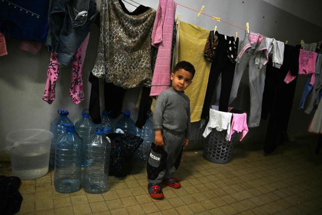 A displaced toddler stands by the laundry of his family at a corridor in a school transformed into a displaced reception center in the area of Dekwaneh, east of Beirut on April 15, 2026. United Nations refugee chief Barham Salih on April 15 called on the international community to provide urgent support to Lebanon, with a fifth of the country's population displaced by the Israel-Hezbollah war. (Photo by Joseph EID / AFP)