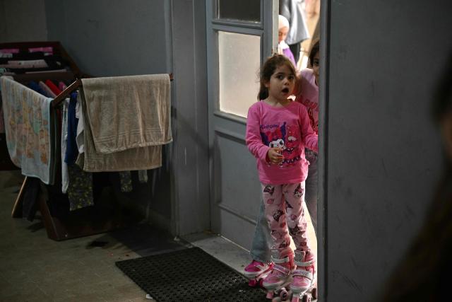 Displaced girls peep-out from the door of a classroom where they reside in a school transformed into a displaced reception center in the area of Dekwaneh, east of Beirut on April 15, 2026. United Nations refugee chief Barham Salih on April 15 called on the international community to provide urgent support to Lebanon, with a fifth of the country's population displaced by the Israel-Hezbollah war. (Photo by Joseph EID / AFP)
