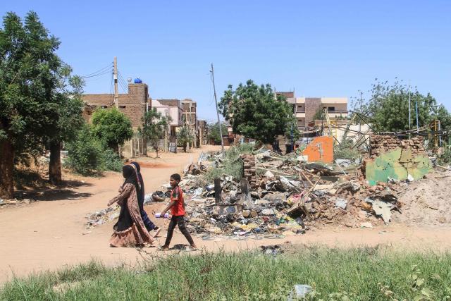 People walk past the rubble of a building in the capital Khartoum on April 15, 2026, on the third anniversary of the start of the war between the army and its paramilitary foes. On the third anniversary of the start of the grinding conflict on April 15, donors will gather in Berlin for an international conference aimed at reviving faltering peace talks and mobilising aid for one of the world's worst humanitarian crises. (Photo by Ebrahim Hamid / AFP)