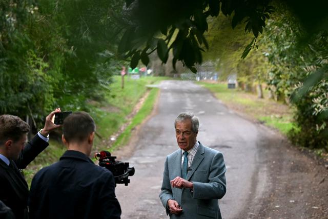Reform UK party leader Nigel Farage speaks to camera outside the entrance to Crowborough military barracks which houses illegal migrants, during his walkabout to campaign in the town of Crowborough, south-east England on April 15, 2026, ahead of local elections on May 7. (Photo by JUSTIN TALLIS / AFP)