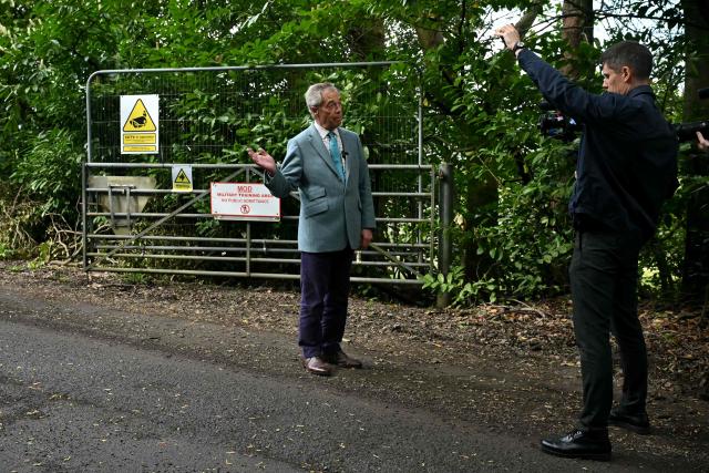 Reform UK party leader Nigel Farage speaks to camera outside the entrance to Crowborough military barracks which houses illegal migrants, during his walkabout to campaign in the town of Crowborough, south-east England on April 15, 2026, ahead of local elections on May 7. (Photo by JUSTIN TALLIS / AFP)