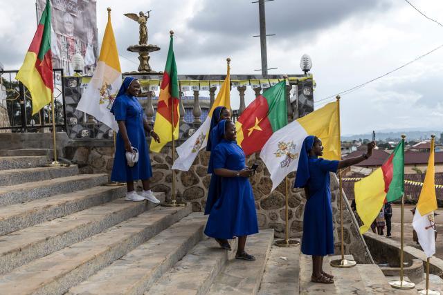 Catholic nuns take a selfie next to Cameroon and Vatican flags at Saint Joseph Metropolitan Cathedral in Bamenda, on April 15, 2026, on the eve of Pope Leo XIV’s visit to Bamenda. (Photo by PATRICK MEINHARDT / AFP)