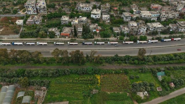 An aerial photograph shows a long line of Iraqi diesel-laden tanker trucks lined up along the Tartus-Baniyas highway as they wait to unload their cargo at the Baniyas port refinery on the Mediterranean Sea, on April 15, 2026. Iraq has begun exporting crude using tanker trucks through Syria, its oil ministry said, as an official said oil revenue last month dropped more than 70 percent compared to February. More than a month into the Middle East war that has wrought havoc on energy markets, Iraq has been particularly impacted as oil exports account for some 90 percent of its budget revenues. Until Iranian attacks and threats all but shut the Strait of Hormuz in revenge for US-Israeli strikes, Iraq exported the majority of its oil through the strategic waterway. (Photo by Bakr ALkasem / AFP)