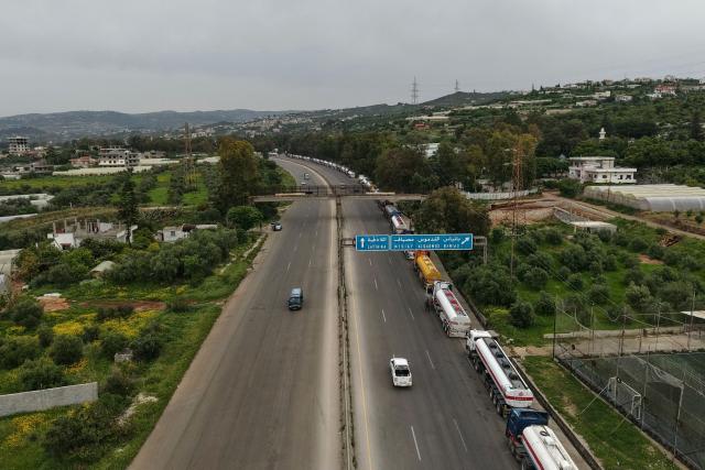 An aerial photograph shows a long line of Iraqi diesel-laden tanker trucks lined up along the Tartus-Baniyas highway as they wait to unload their cargo at the Baniyas port refinery on the Mediterranean Sea, on April 15, 2026. Iraq has begun exporting crude using tanker trucks through Syria, its oil ministry said, as an official said oil revenue last month dropped more than 70 percent compared to February. More than a month into the Middle East war that has wrought havoc on energy markets, Iraq has been particularly impacted as oil exports account for some 90 percent of its budget revenues. Until Iranian attacks and threats all but shut the Strait of Hormuz in revenge for US-Israeli strikes, Iraq exported the majority of its oil through the strategic waterway. (Photo by Bakr ALkasem / AFP)