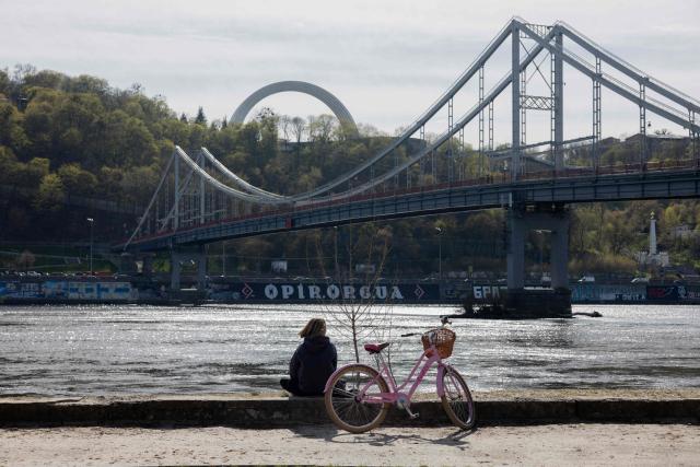 A local resident sits on the banks of the Dnipro River by the Trukhaniv Island in Kyiv on April 15, 2026, amid the Russian invasion of Ukraine. (Photo by Tetiana DZHAFAROVA / AFP)