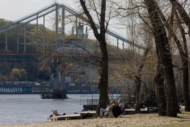 Local residents sit on the banks of the Dnipro River by the Trukhaniv Island in Kyiv on April 15, 2026, amid the Russian invasion of Ukraine. (Photo by Tetiana DZHAFAROVA / AFP)