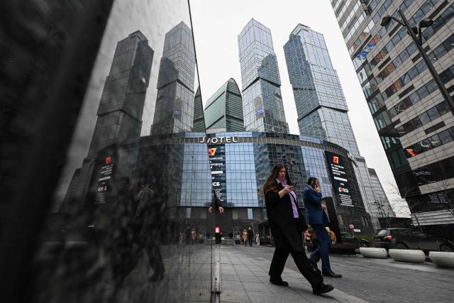 People with mobile phones in their hands walk past the Moscow City business centrein Moscow on April 15, 2026. (Photo by Igor IVANKO / AFP)