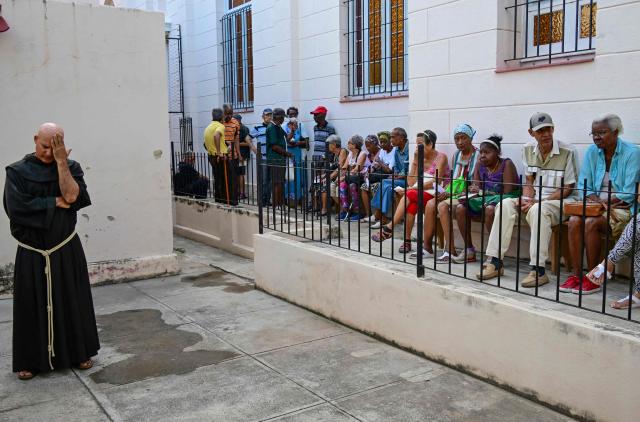Fray Luis Pernas gestures next to elderly people lining up to receive free medicine as social assistance at the Church of the Holy Cross of Jerusalem in Havana on April 14, 2026. Dozens of people, mainly elderly and low income persons, come to this church to receive free medicines they cannot find in pharmacies or hospitals, reflecting the social role churches are playing in a Cuba in crisis. (Photo by YAMIL LAGE / AFP)