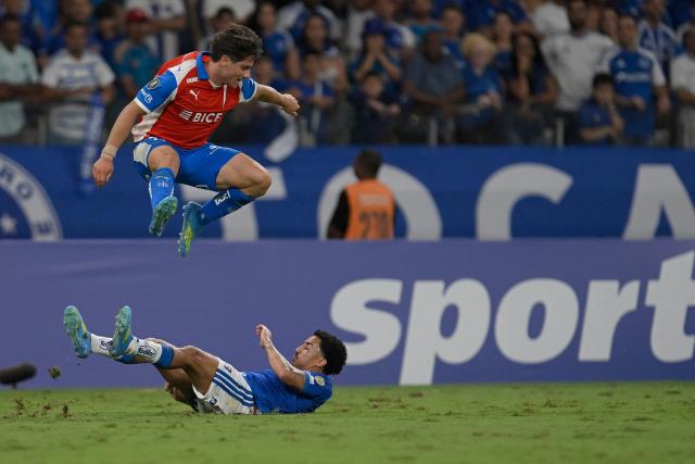Universidad Catolica's forward #11 Clemente Montes leaps over Cruzeiro's midfielder Christian during the Copa Libertadores group stage football match between Brazil's Cruzeiro and Chile's Universidad Catolica at the Mineirao stadium in Belo Horizonte, state of Minas Gerais, Brazil, on April 15, 2026. (Photo by DOUGLAS MAGNO / AFP)