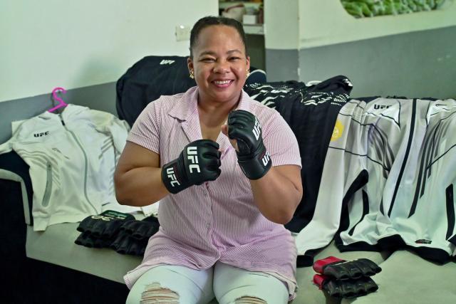 Katty Hurtado, mother of Ecuadorian mixed martial arts fighter Michael Morales, poses for a photo wearing his gloves in Pasaje, El Oro province, Ecuador on April 4, 2026. In a tropical town in Ecuador, children no longer dream only of becoming football players to escape poverty. They also want to be UFC fighters like Michael "Spiderman" Morales, a beast in the octagon who has become a local idol. The 26-year-old fighter has been immortalized in murals and is now the hero of the children on the streets of Pasaje, a town ravaged by violence. (Photo by Marcos PIN / AFP)