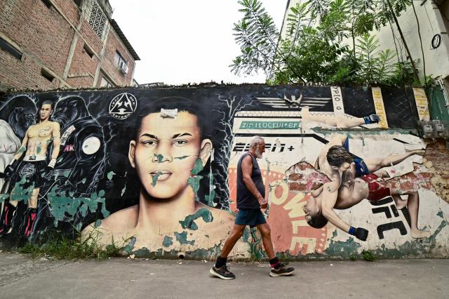 A man walks past a mural depicting Ecuadorian mixed martial arts fighter Michael Morales in Pasaje, El Oro province, Ecuador on April 4, 2026. In a tropical town in Ecuador, children no longer dream only of becoming football players to escape poverty. They also want to be UFC fighters like Michael "Spiderman" Morales, a beast in the octagon who has become a local idol. The 26-year-old fighter has been immortalized in murals and is now the hero of the children on the streets of Pasaje, a town ravaged by violence. (Photo by Marcos PIN / AFP)