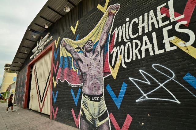 A man walks past a mural depicting Ecuadorian mixed martial arts fighter Michael Morales outside his former training gym in Machala, El Oro province, Ecuador on April 4, 2026. In a tropical town in Ecuador, children no longer dream only of becoming football players to escape poverty. They also want to be UFC fighters like Michael "Spiderman" Morales, a beast in the octagon who has become a local idol. The 26-year-old fighter has been immortalized in murals and is now the hero of the children on the streets of Pasaje, a town ravaged by violence. (Photo by Marcos PIN / AFP)
