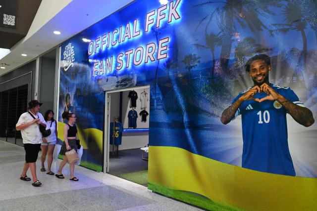 People enter the official fan store, with an image of Curacao's player Leandro Bacuna, in Willemstad, Curacao, in the Dutch Caribbean, on April 8, 2026. Small island, big dreams. The poster of Curacao’s national football team hangs at the entrance of Marchena, a working-class neighborhood of Willemstad, the capital of the smallest territory ever to qualify for a World Cup. (Photo by Raul ARBOLEDA / AFP)