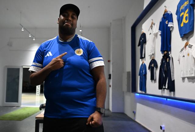 A man tries on a jersey of the Curacao national football team at the official fan store in Willemstad, Curacao, in the Dutch Caribbean, on April 8, 2026. Small island, big dreams. The poster of Curacao’s national football team hangs at the entrance of Marchena, a working-class neighborhood of Willemstad, the capital of the smallest territory ever to qualify for a World Cup. (Photo by Raul ARBOLEDA / AFP)