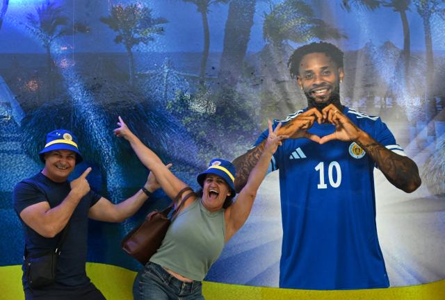 People pose with an image of Curacao's player Leandro Bacuna at the official fan store in Willemstad, Curacao, in the Dutch Caribbean, on April 8, 2026. Small island, big dreams. The poster of Curacao’s national football team hangs at the entrance of Marchena, a working-class neighborhood of Willemstad, the capital of the smallest territory ever to qualify for a World Cup. (Photo by Raul ARBOLEDA / AFP)