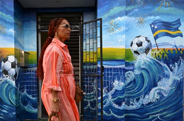 A woman walks past a mural depicting a football and a flag of Curacao in Willemstad, in the Dutch Caribbean, on April 10, 2026. Small island, big dreams. The poster of Curacao’s national football team hangs at the entrance of Marchena, a working-class neighborhood of Willemstad, the capital of the smallest territory ever to qualify for a World Cup. (Photo by Raul ARBOLEDA / AFP)