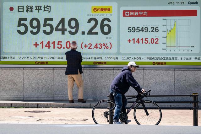 A man (L) looks an electronic quotation board displaying the Nikkei Stock Average on the Tokyo Stock Exchange along a street in Tokyo on April 16, 2026. Japan's Nikkei index surged more than two percent on April 16 to hit a fresh record on optimism about an accord in the US-Iran conflict. (Photo by Yuichi YAMAZAKI / AFP)