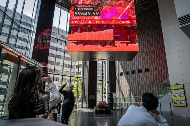 A man has his photograph taken with an electronic quotation board displaying the Nikkei Stock Average on the Tokyo Stock Exchange in Tokyo on April 16, 2026. Japan's Nikkei index surged more than two percent on April 16 to hit a fresh record on optimism about an accord in the US-Iran conflict. (Photo by Yuichi YAMAZAKI / AFP)