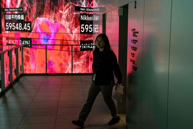 A woman walks past an electronic quotation board displaying the Nikkei Stock Average on the Tokyo Stock Exchange in Tokyo on April 16, 2026. Japan's Nikkei index surged more than two percent on April 16 to hit a fresh record on optimism about an accord in the US-Iran conflict. (Photo by Yuichi YAMAZAKI / AFP)