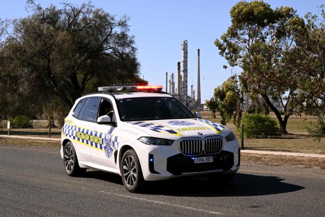 A police car blocks the road leading to the Viva Oil Refinery in Geelong on April 16, 2026 following an overnight fire with authorities warning of disruptions to domestic fuel supply. Towering columns of fire have engulfed a crucial Australian oil refinery after a chain of explosions, authorities said on April 16 as they warned of disruptions to domestic fuel supply. (Photo by William WEST / AFP)