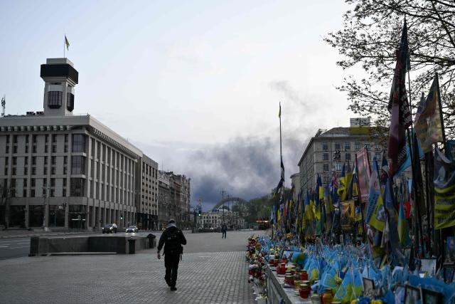 A person walks along a street as smoke rises over Kyiv following a Russian strike on April 16, 2026, amid the Russian invasion of Ukraine. Russian strikes killed at least 12 people in Ukraine, local authorities said on April 16, after Moscow pummelled its neighbour in overnight attacks. (Photo by Genya SAVILOV / AFP)
