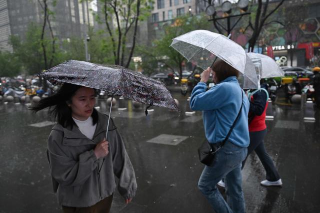 People use umbrellas to protect themselves from the rain in Beijing on April 16, 2026. (Photo by Pedro PARDO / AFP)