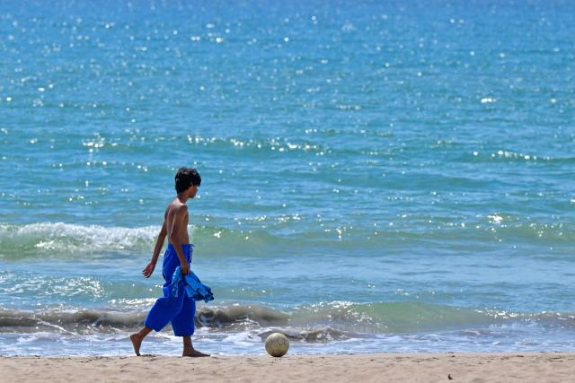 A boy plays football along a beach in Trincomalee on April 16, 2026. (Photo by Ishara S. KODIKARA / AFP)