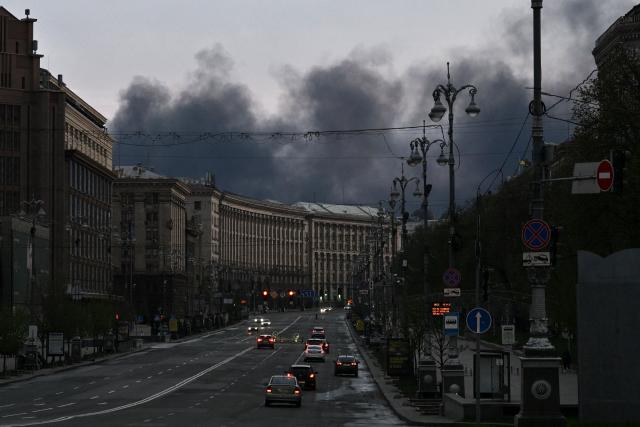 Cars drive along Khreshchatyk Street as smoke rises above buildings in the background following an air attack in Kyiv on April 16, 2026. Russian forces launched hundreds of drones and dozens of missiles at cities across Ukraine, Kyiv's air force announced on April 16, 2026, in a barrage that killed at least 14 people. (Photo by Genya SAVILOV / AFP)