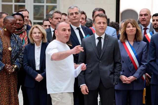France's President Emmanuel Macron (R) listens to French raper Virus, next to French Culture Minister Catherine Pegard (2ndL) and French radio host Aline Afanoukoe (L) upon his arrival at the International City of French Language (Cite Internationale de la Langue Francaise) to promote 'disconnecting' and 'reading' as alternatives to screens as part of his fight to ban social networks for the youngest in the castle of Villers-Cotterets, northern France on April 16, 2026. In response to the explosion in screen time among 6- to 17-year-olds and the impact of algorithms on our children, Emmanuel Macron has pledged to ban social media for those under 15. (Photo by Ludovic MARIN / POOL / AFP)