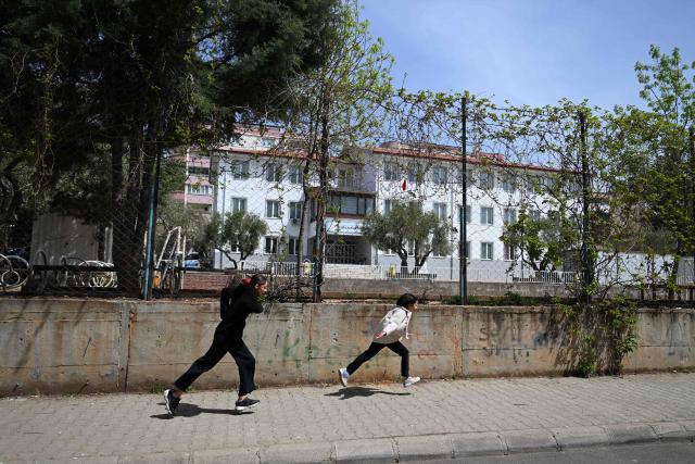 Two girls runs outside of the Ayser Calik college, ahead of the funerals for nine victims killed in a school shooting by a 14-year-old, an attack that has sent shockwaves across the country, with authorities saying the suspect had referenced a US mass killer in a WhatsApp profile image, in the southern province of Kahramanmaras on April 16, 2026. The funerals take place for eight children aged 10 and 11 and a 55-year-old teacher. (Photo by YASIN AKGUL / AFP)