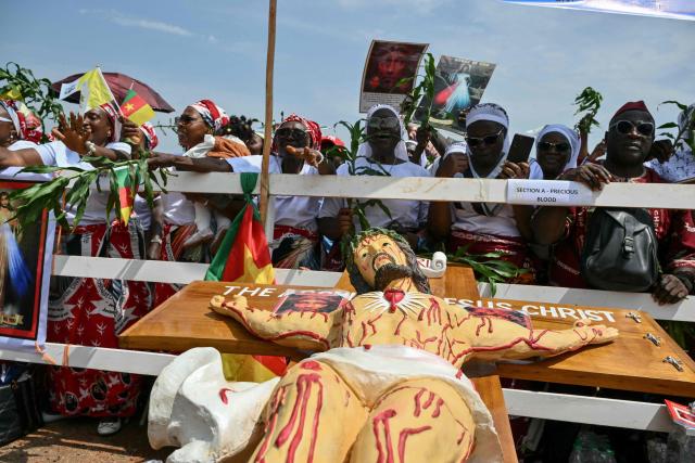 A general view of a crucifix near supporters of Pope Leo XIV cheering as they wait for his arrival at Saint Joseph's Cathedral in Bamenda, on the fourth day of an 11-day apostolic journey to Africa, on April 16, 2026. (Photo by Alberto PIZZOLI / AFP)