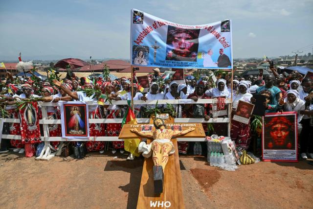 A general view of a crucifix near supporters of Pope Leo XIV cheering as they wait for his arrival at Saint Joseph's Cathedral in Bamenda, on the fourth day of an 11-day apostolic journey to Africa, on April 16, 2026. (Photo by Alberto PIZZOLI / AFP)