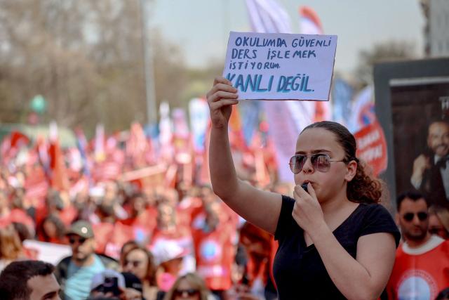 Teachers and members of education unions march as a protester hold a placard which reads "I want to teach safely at my school." during a protest against school shootings, in Ankara on April 16, 2026. More than 3,500 teachers from several education unions protested in the Turkish capital Ankara on  following deadly school shootings, calling for the resignation of the education minister. (Photo by ADEM ALTAN / AFP)