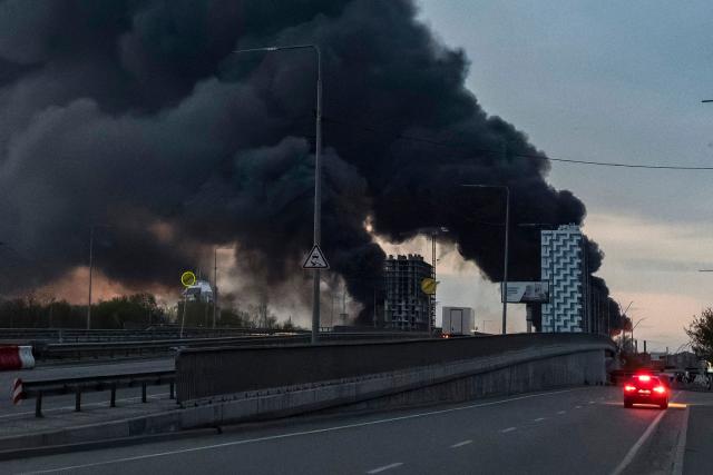 A car drives along the street as smoke rises above buildings following an air attack in Kyiv on April 16, 2026, amid the Russian invasion of Ukraine. A massive Russian drone and missile barrage killed at least 16 people in cities across Ukraine, more than four years into the war with peace talks stalled, Ukrainian officials said on April 16, 2026. (Photo by Vladyslav Musiienko / AFP)