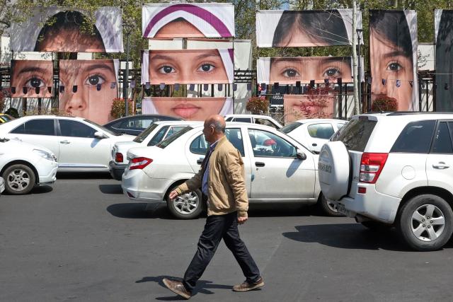 A man walks past the portraits of children killed in a deadly strike on a children’s school in the southern city of Minab on the first day of the war that killed at least 165 people, most of them children, at the Tajrish Square in Tehran on April 16, 2026. The military adviser to Iran's supreme leader Mojtaba Khamenei on April 15 warned that Iran would sink American ships in the Strait of Hormuz if the United States decided to "police" the key shipping bottleneck. (Photo by AFP) / 