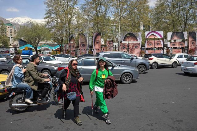 Commuters make their way past the portraits of children killed in a deadly strike on a children’s school in the southern city of Minab on the first day of the war that killed at least 165 people, most of them children, at the Tajrish Square in Tehran on April 16, 2026. The military adviser to Iran's supreme leader Mojtaba Khamenei on April 15 warned that Iran would sink American ships in the Strait of Hormuz if the United States decided to "police" the key shipping bottleneck. (Photo by AFP) / 
