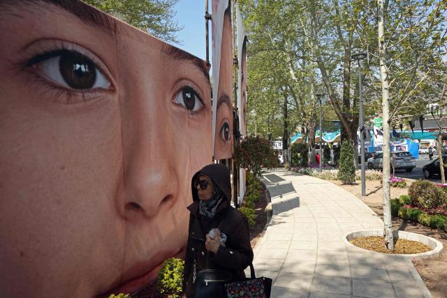 A woman walks past the portraits of children killed in a deadly strike on a children’s school in the southern city of Minab on the first day of the war that killed at least 165 people, most of them children, at the Tajrish Square in Tehran on April 16, 2026. The military adviser to Iran's supreme leader Mojtaba Khamenei on April 15 warned that Iran would sink American ships in the Strait of Hormuz if the United States decided to "police" the key shipping bottleneck. (Photo by AFP) / 