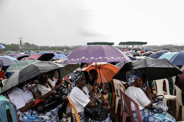 Attendees shelter themselves from the rain with umbrellas as they wait for Pope Leo XIV to arrive to lead the Holy Mass at Bamenda Airport in Bamenda, on the fourth day of an 11-day apostolic journey to Africa, on April 16, 2026. (Photo by Patrick MEINHARDT / AFP)