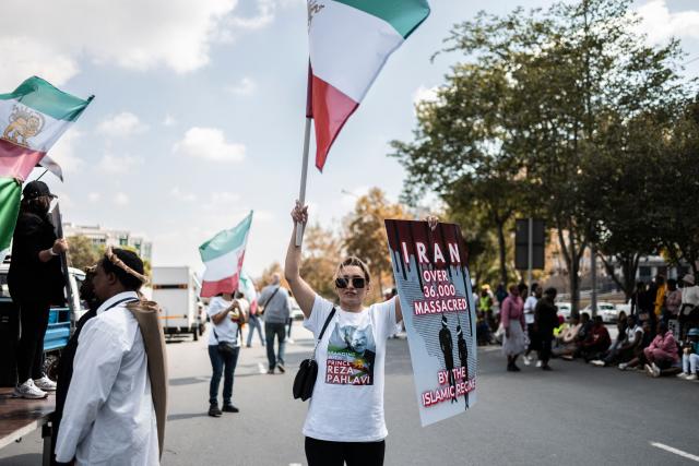 An Iranian pro-democracy activist waves the pre-1979 Iranian national flag and a placard during a protest in front of the US Consulate in Sandton, on April 16, 2026. (Photo by ILARIA FINIZIO / AFP)