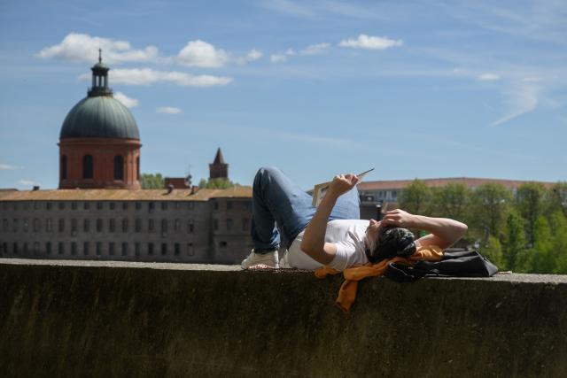 A man reads a book on a wall beside the Garonne river with a view of the Chapelle Saint-Joseph de la Grave in Toulouse, southern France, on April 16, 2026. (Photo by Ed JONES / AFP)