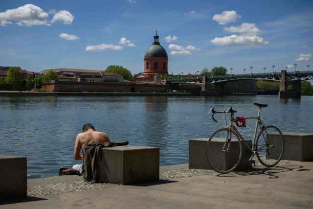 A man sits before the Garonne river with a view of the Chapelle Saint-Joseph de la Grave in Toulouse, southern France, on April 16, 2026. (Photo by Ed JONES / AFP)