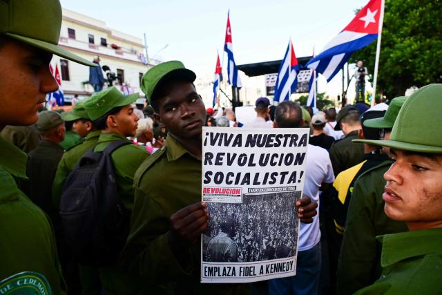 A member of the Ministry of the Interior holds a poster reading "Long live our socialist revolution" during celebrations marking the 65th anniversary of the Declaration of the Socialist Character of the Cuban Revolution by late leader Fidel Castro in the El Vedado neighborhood of Havana on April 16, 2026. (Photo by YAMIL LAGE / AFP)