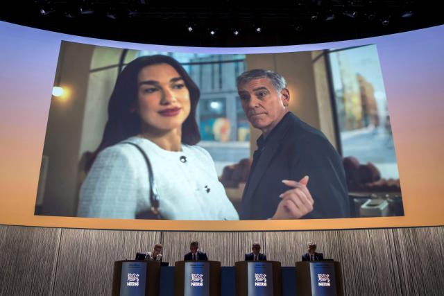 An advertisement for Nespresso coffee brand showing English singer and songwriter Dua Lipa (L) and US actor and filmmaker George Clooney is displayed on a giant screen ahead of Swiss food giant Nestle's annual general meeting in Ecublens near Lausanne, on April 16, 2026. (Photo by Fabrice COFFRINI / AFP)