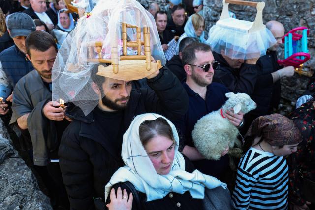 Pilgrims, including childless couples, with toy cradles participate in the Tsachkhuroba pilgrimage to the hill-sit Archangel monastery to pray God and ask for mercy and for a child, in the village of Tsachkhuri on April 16, 2026. Thousands joined the 3 km uphill monastery procession in an annual fertility pilgrimage, happening on Thursday of the week following Orthodox Easter. (Photo by Giorgi ARJEVANIDZE / AFP)