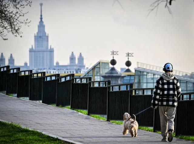 A girl walks a dog in front of the Moscow State University on April 16, 2026. (Photo by Alexander NEMENOV / AFP)