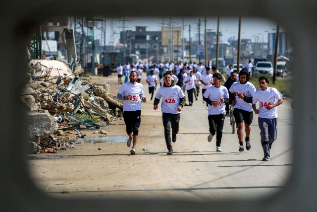 TOPSHOT - Palestinians run past damaged buildings during a marathon organised by the UAE-based foundation Al-Faris al-Shahm at the Bureij camp for internally displaced people in the central Gaza Strip on March 27, 2026. Violence has persisted in Gaza despite a ceasefire in October 2025, with both Israel and Hamas regularly accusing each other of violations. (Photo by Eyad Baba / AFP)